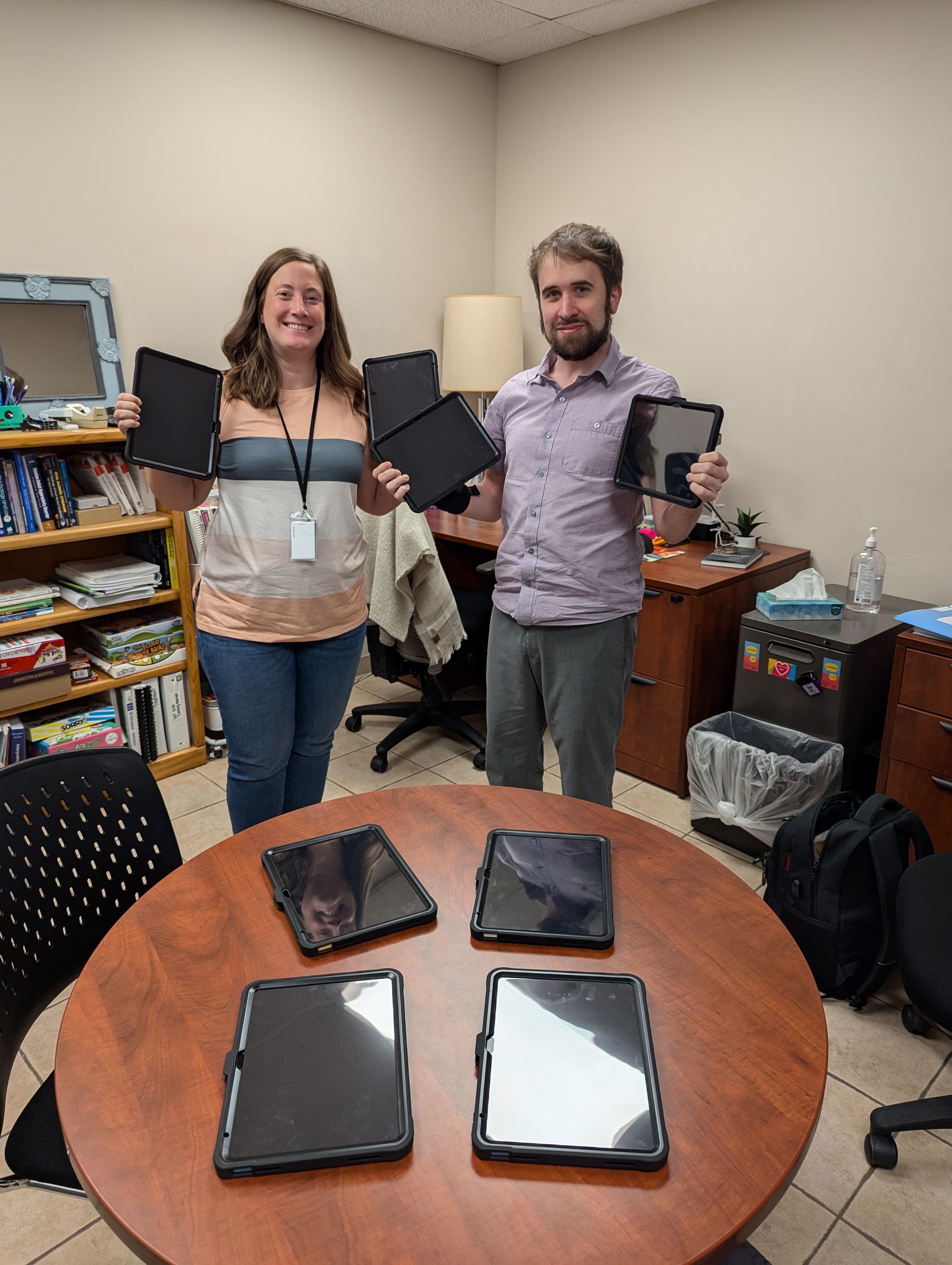 A man and a woman each holding an iPad with four iPads on a table.